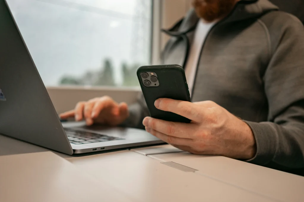 A salon owner managing online bookings from a phone while using a laptop
